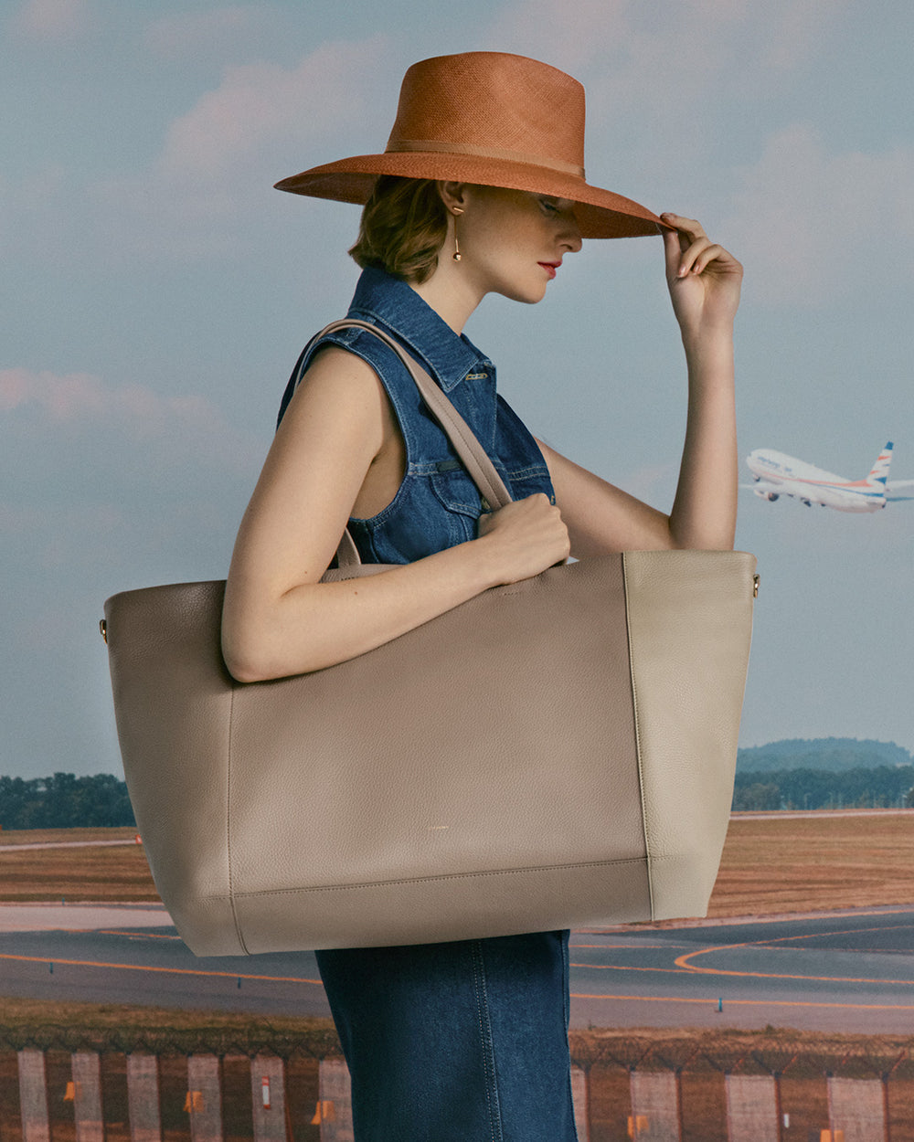 Easy Overnighter Bag Person holding a large bag standing in front of a runway with a plane in the background, wearing a hat.