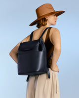 Woman wearing a hat and carrying a backpack, looking away from the camera.