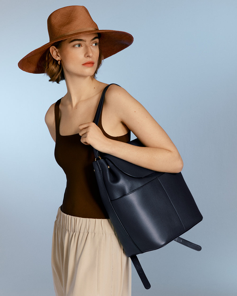 Woman wearing a hat and tank top, carrying a shoulder bag, looking to the side.