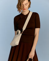 Woman in a polo shirt and skirt carrying a shoulder bag.