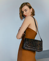Woman posing with a shoulder bag, looking over her shoulder.
