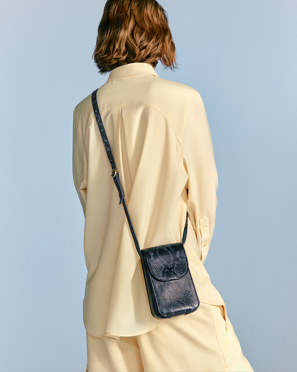Person wearing an outfit with a shoulder bag, viewed from the back.