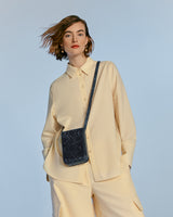 Woman in buttoned shirt and pants with a crossbody bag, hair blowing