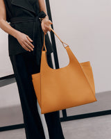 Person holding a large handbag, standing next to a wall.