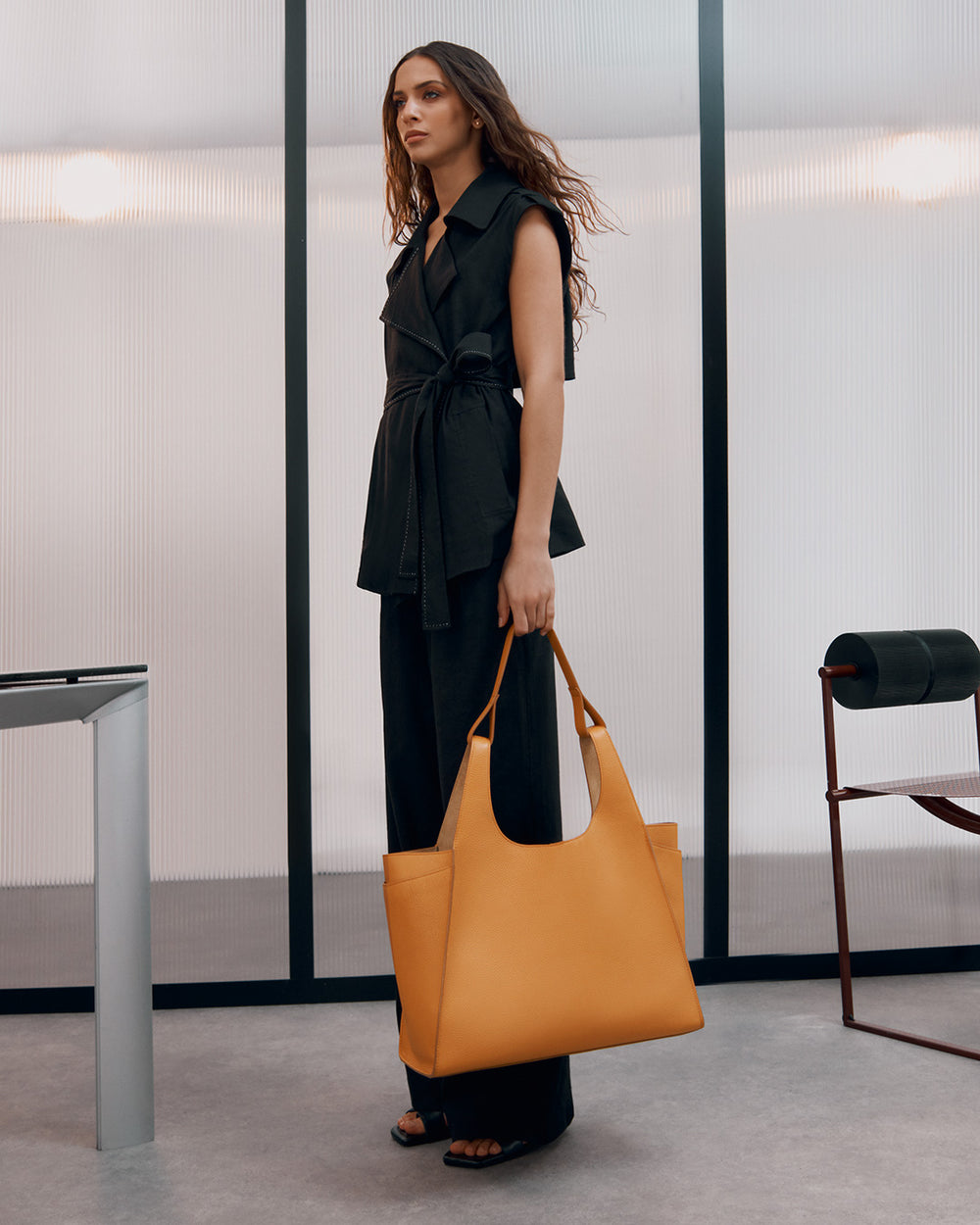 Woman standing in a room holding a large handbag.