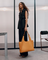 Woman standing in a room holding a large handbag.