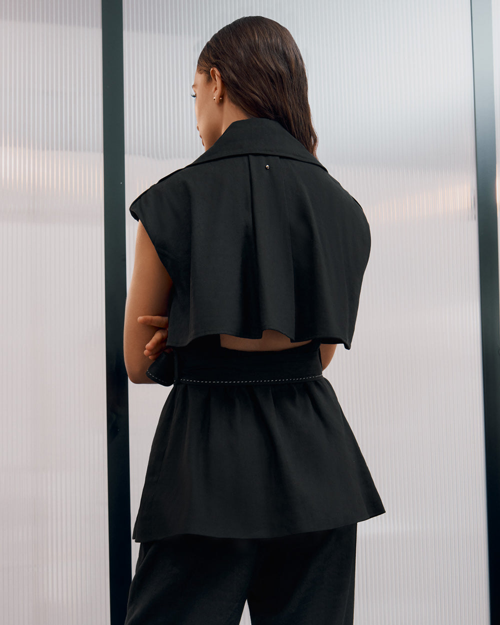 Linen Vest Woman in a cropped top and pants viewed from the back, standing near a window.