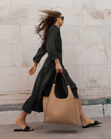 Woman walking briskly with a large bag and sunglasses.