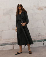 Woman standing in dress and sandals against a marble wall.