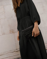 Woman holding a clutch bag, standing near a wall.