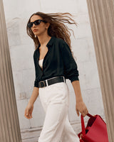 Woman walking by a column while holding a red bag.