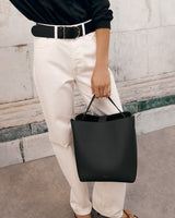 Person holding a bucket bag and wearing pants with a belt