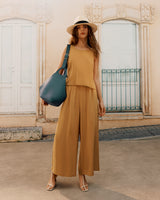 Woman standing in front of a building wearing a sleeveless outfit, hat, and holding a large bag
