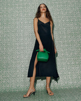 Woman in long dress holding a bag, standing against a patterned wall