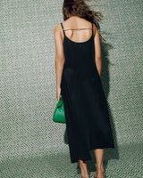 Person in a dress, holding a small bag, standing against a patterned background.