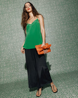 Person in a green top holding an orange clutch bag, standing against a geometric background