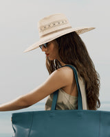 Woman wearing a hat and sunglasses, holding a large travel bag