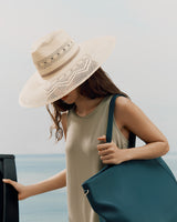Person wearing a sleeveless top and wide-brim hat, holding a large bag.
