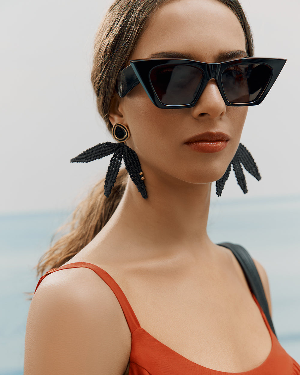 Woman wearing large sunglasses, earrings, and a sleeveless top.