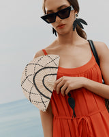Woman in a dress holding a fan, wearing sunglasses and leaf-shaped earrings