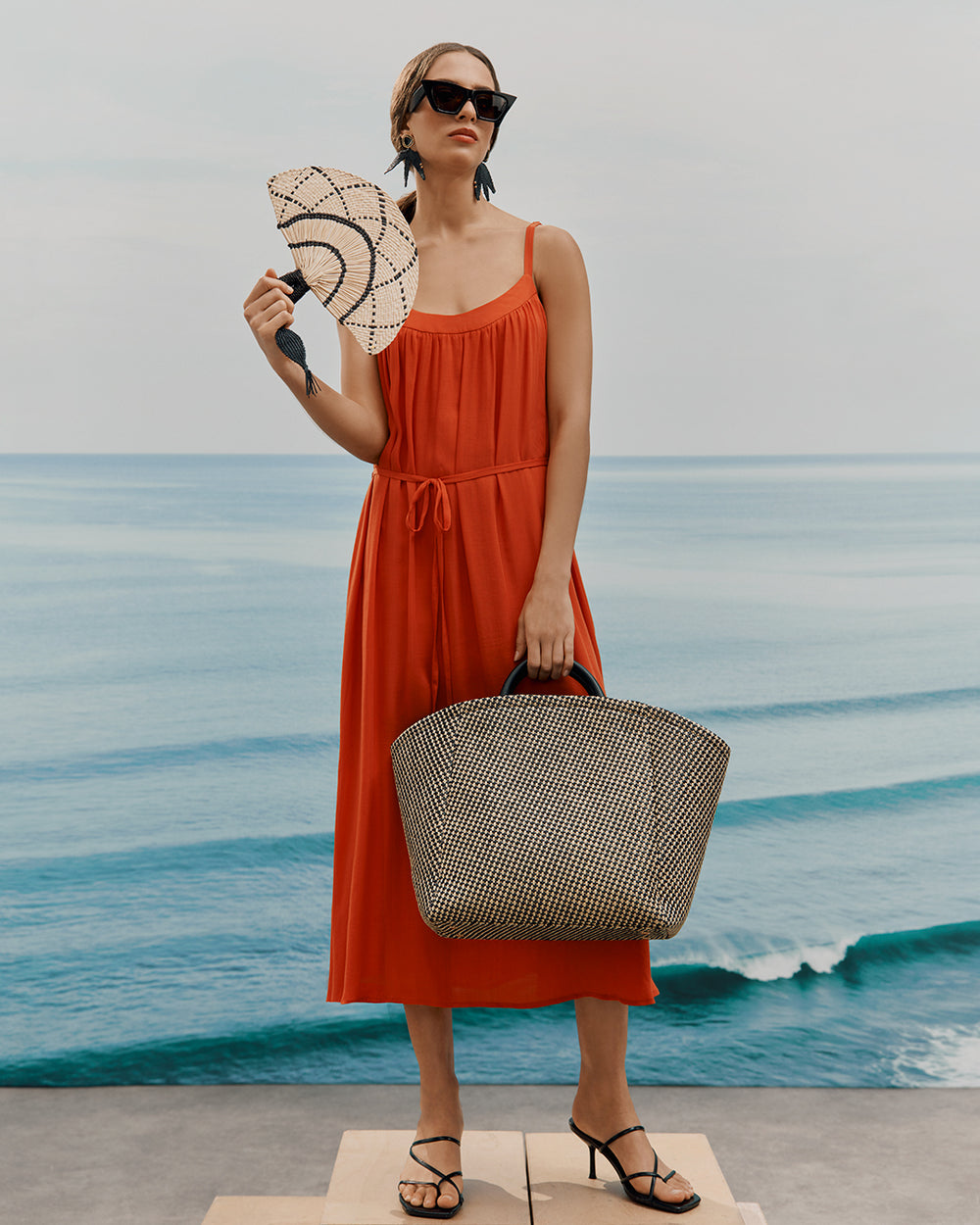 Palma Tote Woman in a dress holding a fan and a bag by the sea.