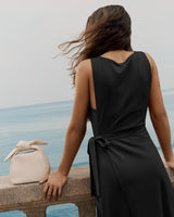 Person in a dress standing by a railing overlooking the sea with a handbag on the ledge.