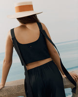 Person standing by a railing, wearing a sleeveless top and a brimmed hat with a ribbon.