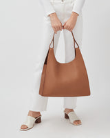 Person holding a large bag, standing in white pants and open-toe shoes.
