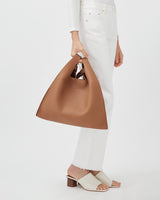 Person standing, holding a large handbag, wearing heeled sandals and high-rise pants.