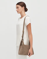 Woman standing side profile with a shoulder bag.