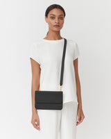 Woman standing with a shoulder bag, looking at the camera.