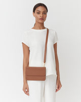 Woman standing with a crossbody bag, looking at the camera.