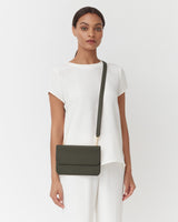 Woman standing and carrying a shoulder bag, looking at the camera.