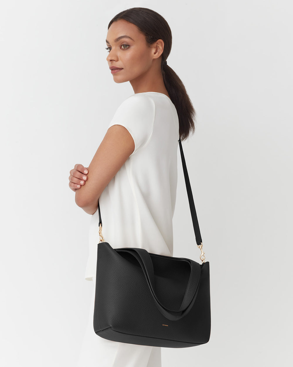 Woman standing with a shoulder bag, looking over her shoulder.