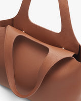 Close-up of a leather tote bag with exterior pockets.