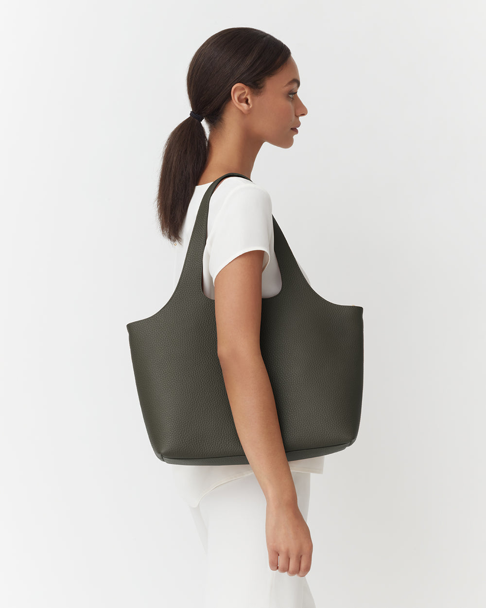 Woman with a ponytail carrying a large tote bag over her shoulder.