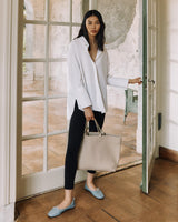 Woman standing by a door holding a bag.