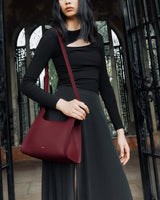 Person holding a shoulder bag, standing near an ornate gate.