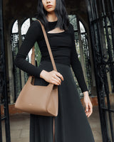 Person holding a shoulder bag, standing near an ornate gate.