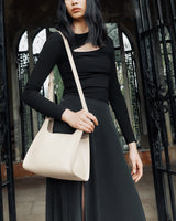 Person holding a shoulder bag, standing near an ornate gate.