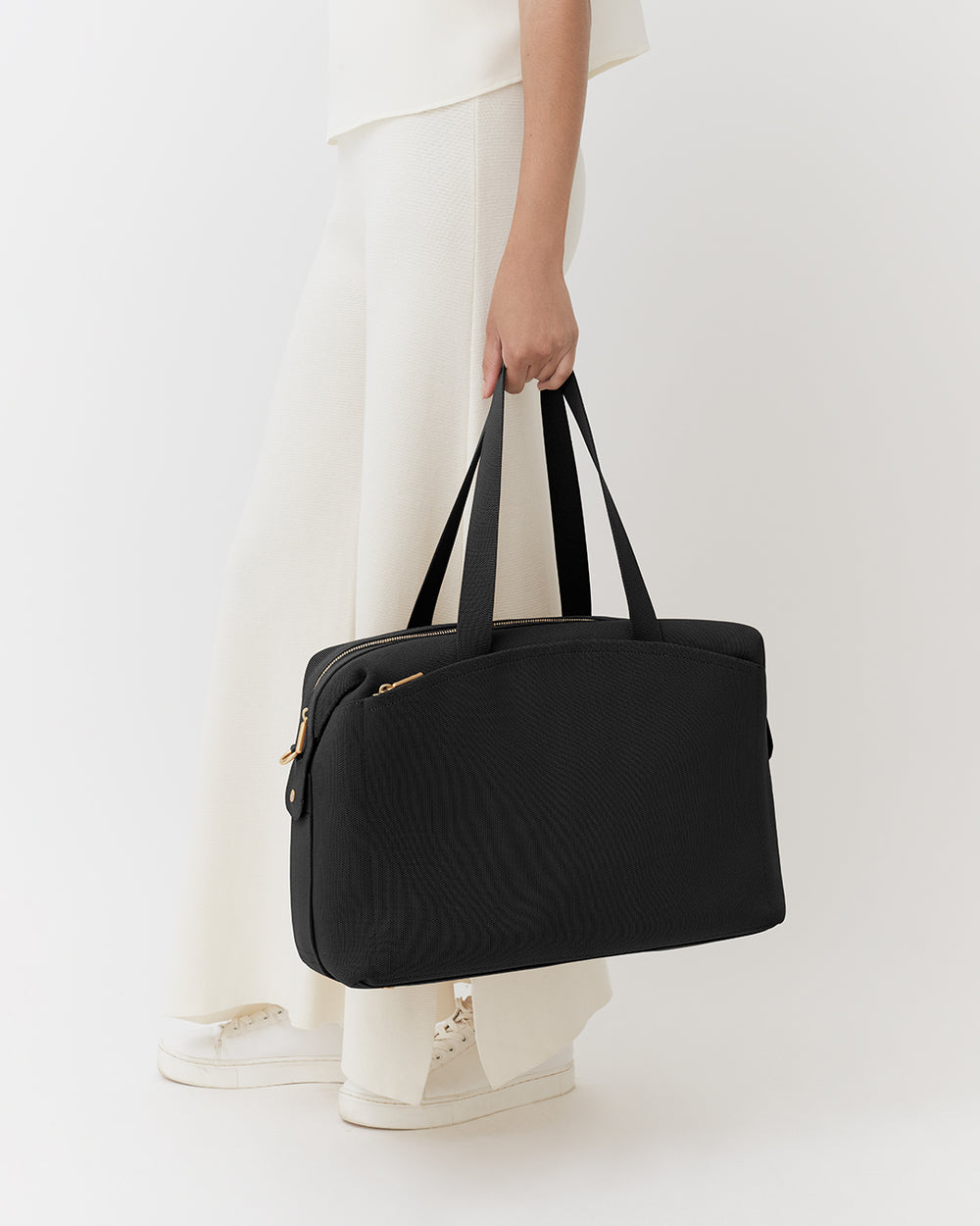 Person holding a travel bag wearing pants and sneakers.