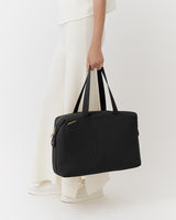Person holding a travel bag wearing pants and sneakers.