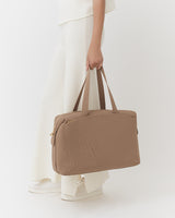 Person holding a travel bag, wearing long pants and shoes.