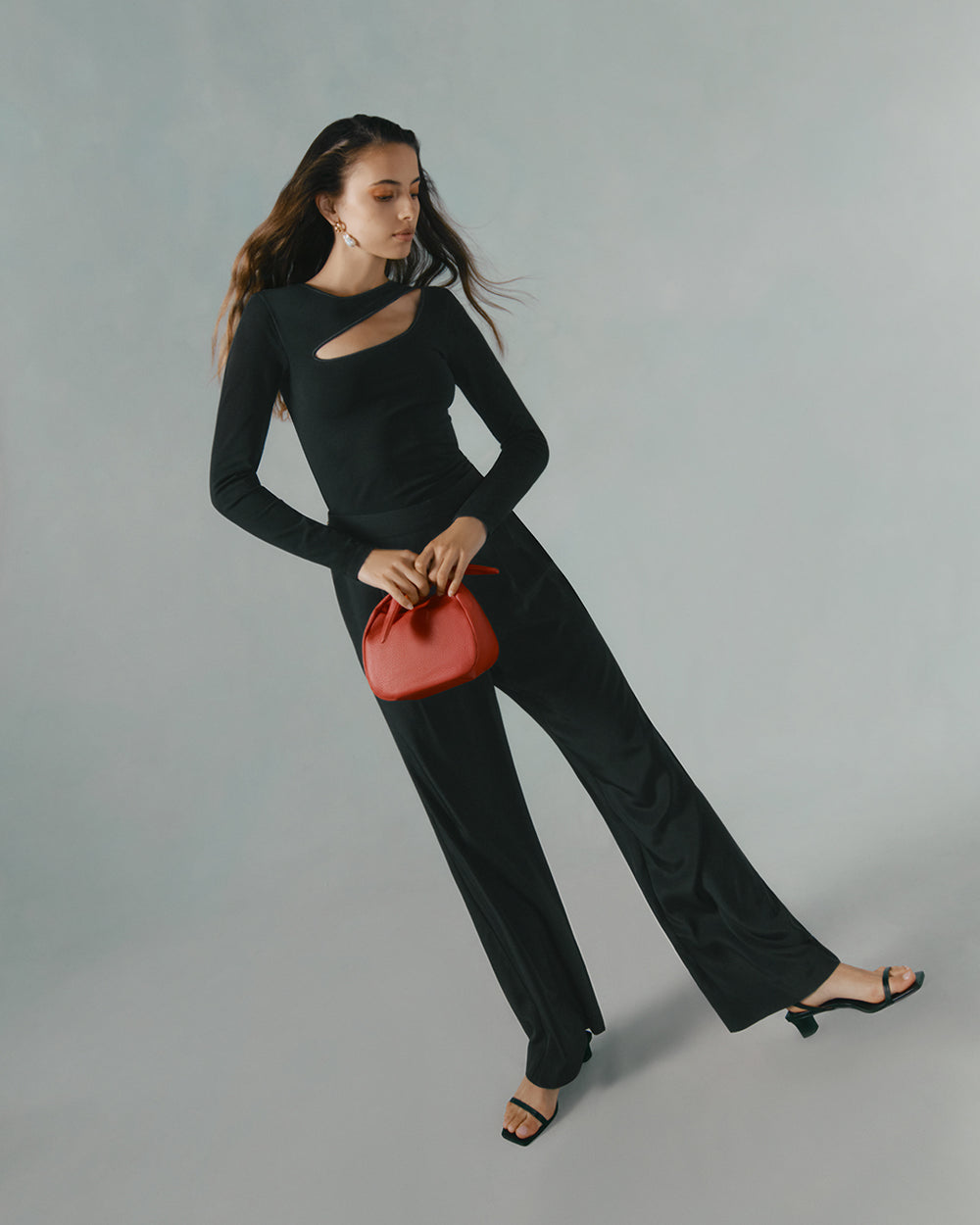 Woman in a long sleeve top and pants holding a small bag.