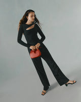 Woman in a long sleeve top and pants holding a small bag.