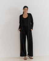 Woman standing against a plain background, wearing a suit and sandals.