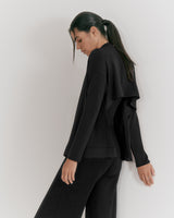 Woman in a loose top and pants standing sideways with head turned.