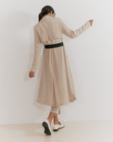 Person in a trench coat and heels walking away and pointing forward.
