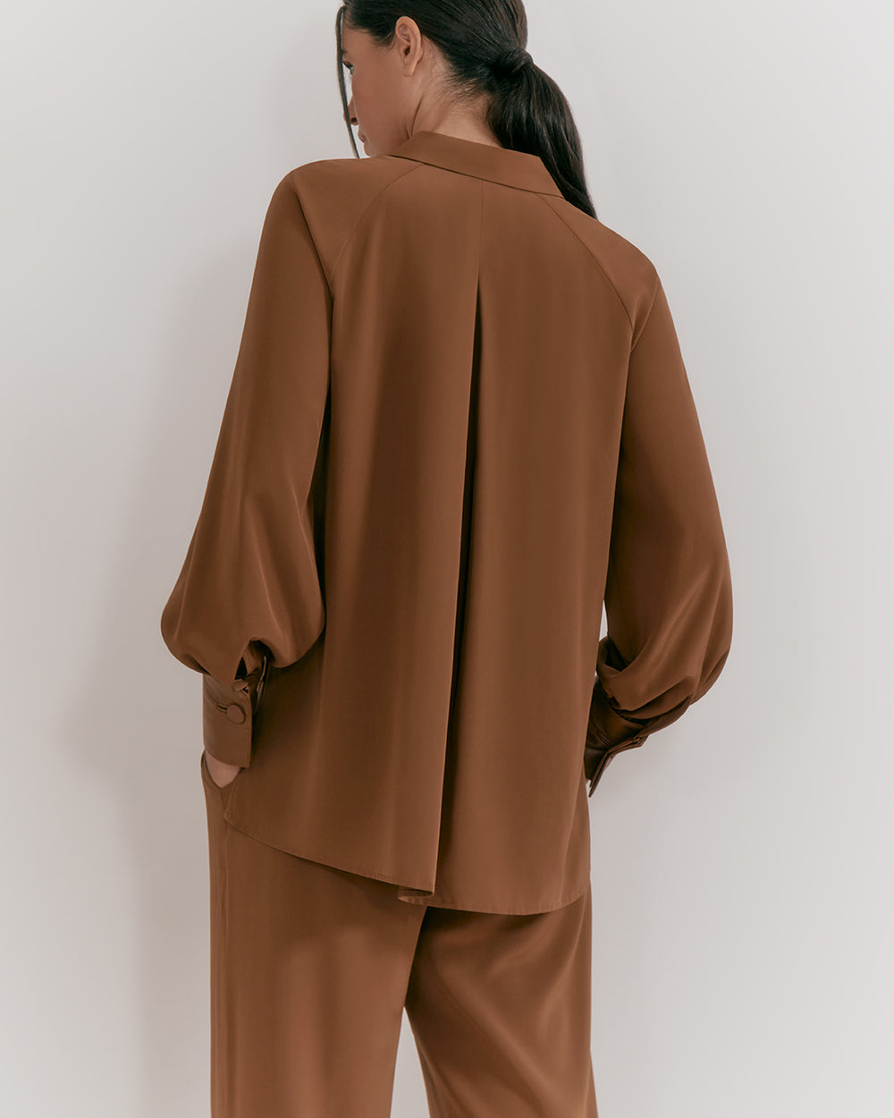 Silk Leather Cuff Shirt Woman standing with her back to the camera, wearing a suit with wide sleeves.