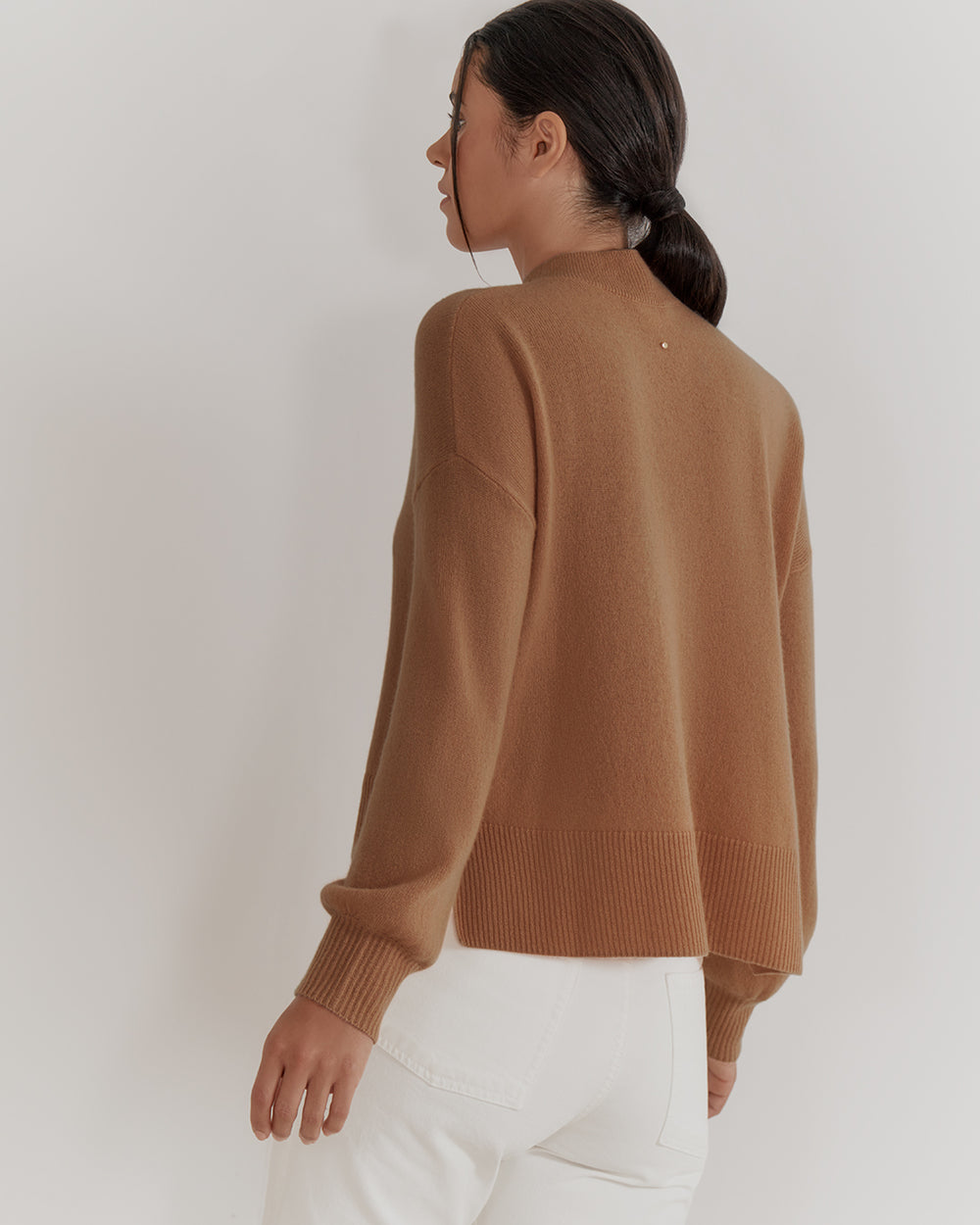 Woman in sweater and pants, viewed from the back, looking to the side.